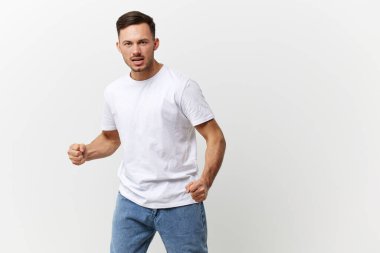 Çığlık atan, kızgın, bronzlaşmış, basit tişörtlü yakışıklı adam beyaz stüdyo arka planında izole edilmiş yumruklarını sıkıyor. Uzayın afiş modelini kopyala. İnsanların duyguları Yaşam tarzı konsepti