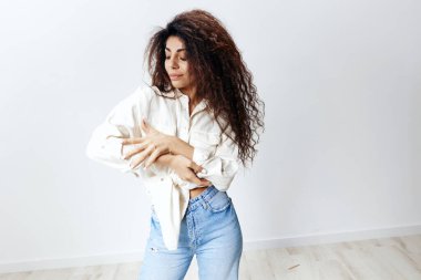 Eco Friendly Fashion Konsepti. Beyaz Flax Shirt 'ün tadını çıkaran, Beyaz Stüdyo Arkaplan' da izole edilmiş eline bakan Afro Saçlı Mutlu Latin Kadın. Banner Mockup kopyalama alanı boş