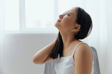 Boyun ağrısı. Fibromiyalji yüzünden acı çeken, bronzlaşmış, güzel, Asyalı bir kadın masaj yapan, gergin kaslarını ovuşturan ev içi oturma odasında. Yaralar Kötü Sağlık Hastalığı konsepti. Güzel teklif Banner.