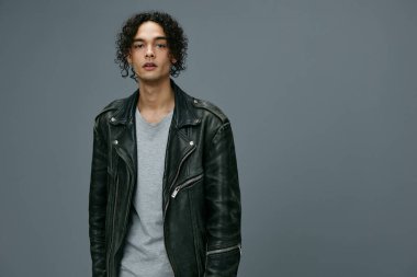 Güzel moda teklifi. Oldukça şık bronzlaşmış kıvırcık deri ceketli adam gri stüdyo arka planında izole edilmiş kameraya bakıyor. Büyük Mevsimlik Satış Yeni Koleksiyon konsepti. İlan için alanı kopyala