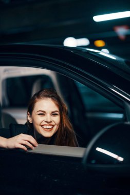 Geceleri, bir kadının arabada oturup pencereden dışarı bakarken, kameraya gülerken ve gözlerini kapatırken çekilmiş dikey bir fotoğrafı. Yüksek kalite fotoğraf