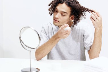 Aynalı cilt bakımının önünde beyaz tişörtlü yakışıklı bir adam izole edilmiş. Yüksek kalite fotoğraf