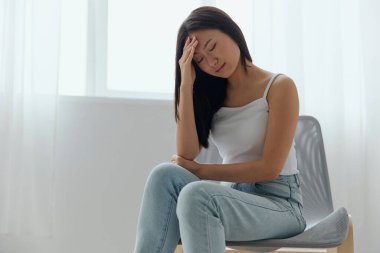 Yüksek sıcaklıklar. Gizli kimlik belirtileri. İşkence görmüş, bronzlaşmış, güzel, Asyalı genç bir bayan. Kafasına dokunuyor. Ev içi oturma odasında baş ağrısı hissediyor. Yaralar Kötü Sağlık Hastalığı konsepti. Güzel teklif Banner.