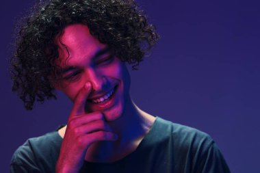 Siyah tişörtlü neşeli kıvırcık adam pembe mavi stüdyo arka planında yalnız poz veriyor. Güzel moda teklifi. Sanal Gerçeklik Yeni Koleksiyon konsepti. İlan için alanı kopyala