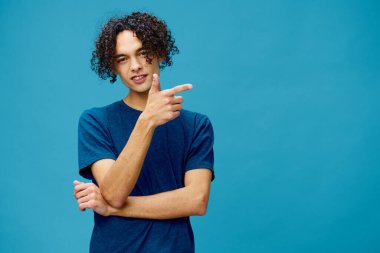 Süper havalı, bronzlaşmış, beyaz tenli, basit tişörtlü adam mavi arka planda yalnız poz veriyor. Yaşam tarzı ve Duygular konsepti. Reklam için fotokopi alanı için iyi teklif.