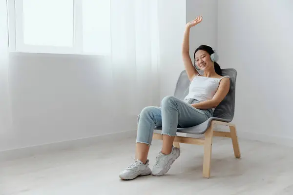 Cheerful happy relaxing tanned lovely young Asian woman in headphones dance move to music at home interior living room. Sound Studio Stream, Social media concept. Cool offer Banner Wide angle