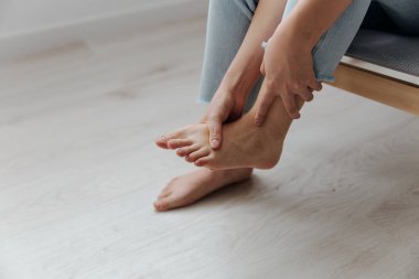 Evdeki oturma odasında bronzlaşmış, genç ve güzel bir Asyalı kadının ayak bileğine dokunuşunu yakından çek. Yaralar Kötü Sağlık Hastalığı konsepti. Güzel teklif Banner.
