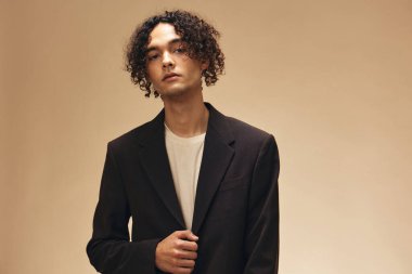 Klasik kahverengi ceketli, solaryum renginde harika kıvırcık bir adam bej renkli pastel arka planda yalnız poz veriyor. Yeni Moda Koleksiyonu teklifi. Retro stil konsepti. Reklam için boş yer