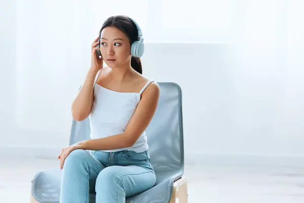 Excited shocked tanned lovely young Asian lady in headphones looks aside listens to external sounds at home interior living room. Sound Studio Stream Social media concept. Cool offer Banner Wide angle