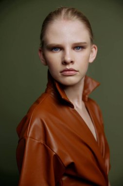 Deri elbiseli, akşam makyajlı, mavi gözlü zarif sarışın kız afiş tasarımı için izole edilmiş poz veren kameraya bakıyor. Yeşil arka planda stüdyo portresi. Makyaj konsepti