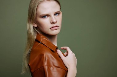 Pankart tasarımı için moda teklifi. Deri cekete dokunan kendine güvenen genç bir kadının yakın plan portresi zeytin yeşili stüdyo arka planındaki kameraya bakıyor. Yüksek kalite fotoğraf