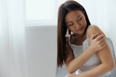 Yanlış pozisyonda uyuduktan sonra nevraljiden muzdarip olan güzel, genç Asyalı bir kadının oturma odasındaki ağrılı omzuna dokunması. Yaralar Kötü Sağlık Hastalığı konsepti. Güzel teklif Banner.