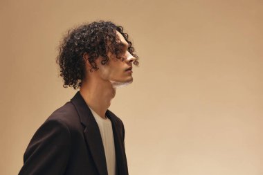 Klasik kahverengi ceketli, solaryum renginde harika kıvırcık bir adam bej renkli pastel arka planda yalnız poz veriyor. Yeni Moda Koleksiyonu teklifi. Retro stil konsepti. Reklam için boş yer