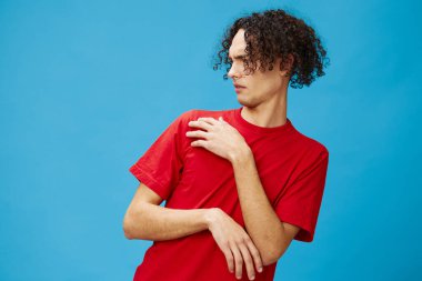 Mutsuz, bronzlaşmış, kırmızı tişörtlü beyaz adam mavi arka planda izole edilmiş, tiksindirici poz veriyor. Yaşam tarzı ve Duygular konsepti. Reklam için fotokopi alanı için iyi teklif.