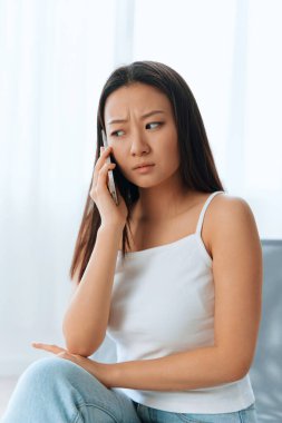 Wary confused attended tanned lovely young Asian woman listen shocked news at call using phone at home interior living room. Distance communication Social media concept. Cool offer Banner Wide angle