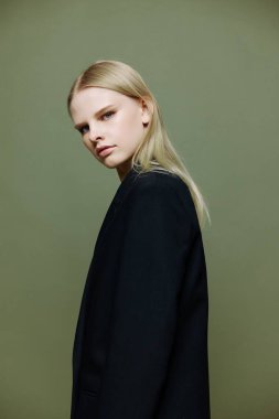 Genç model döner ve omzunun üzerinden kameraya bakar. Güzel pankart teklifi. Stüdyoda yeşil arka planı olan bir kız takım elbiseyle yalnız poz veriyor. Yüksek kalite fotoğraf