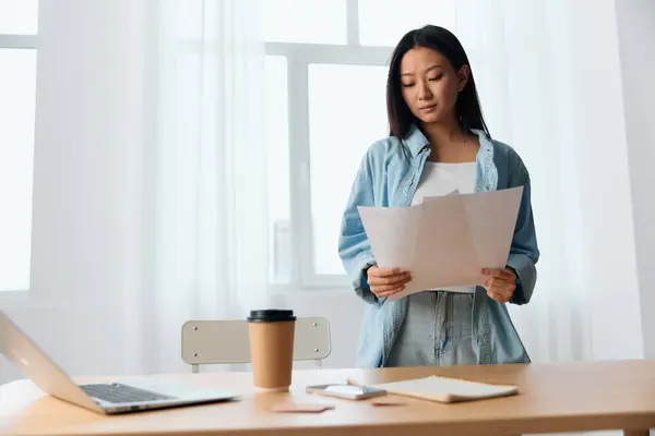 Concentrated thoughtful young Asian cute female businesswoman deals with documents on table with laptop in office interior. Employee work at home. Lady corporation leader concept. Copy space Offer