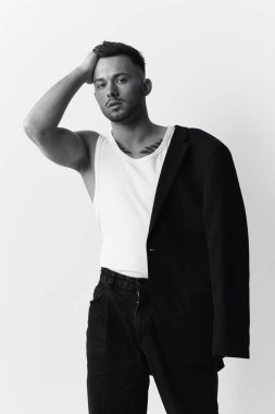 Fotoğrafları modelliyorum. Kendine güveni olan, ceketli, tek omuzlu, yakışıklı bir adam beyaz stüdyo arka planında yalnız poz veriyor. Siyah ve Beyaz konsepti. Moda teklifi. Boşluğu kopyala