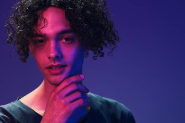Siyah tişörtlü şık kıvırcık adam pembe mavi stüdyo arka planında yalnız poz veren kameraya bakıyor. Güzel moda teklifi. Sanal Gerçeklik Yeni Koleksiyon konsepti. İlan için alanı kopyala