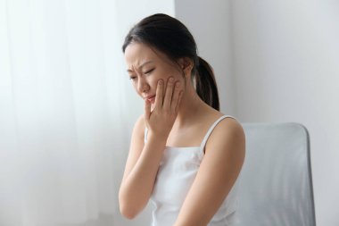 Diş çürüğü, yirmilik diş Pulpitis Periodontiti. Mutsuz, bronzlaşmış, güzel, Asyalı bir kadın oturma odasının iç taraflarına dokunuyor. Yaralar Kötü Sağlık Hastalığı konsepti. Güzel teklif.