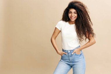 Aşırı neşeli, beyaz tişörtlü, kameraya gülümseyen, el ele tutuşan, izole edilmiş bej arka planı olan bir kadın. Uzay giysileri moda markalarını kopyalayın, ilanınız için bedava yer