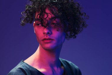 Siyah tişörtlü şık kıvırcık adam pembe mavi stüdyo arka planında yalnız poz veriyor. Güzel moda teklifi. Sanal Gerçeklik Yeni Koleksiyon konsepti. İlan için alanı kopyala