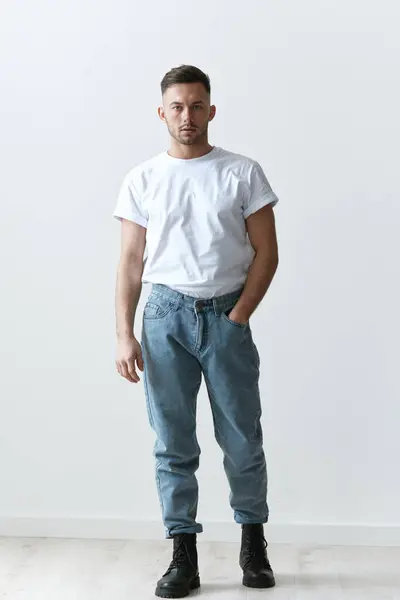 Full body shot of handsome serious tanned man guy in basic t-shirt holds hand on jeans posing on white background. Fashion Style New Collection Offer. Copy space for ad. Modeling snapshots