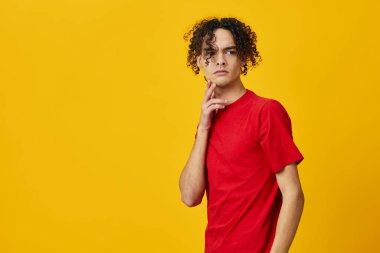 Kafası karışmış kırmızı tişörtlü beyaz bir genç sarı stüdyo arka planında izole bir şekilde poz veremez. Reklamcılık için bedava olan en iyi teklif. Günlük kavramlar için duygular
