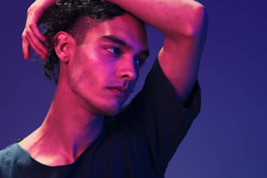 Siyah tişörtlü şık kıvırcık adam pembe mavi stüdyo arka planında yalnız poz veriyor. Güzel moda teklifi. Sanal Gerçeklik Yeni Koleksiyon konsepti. İlan için alanı kopyala