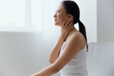 Gıdıklayan öksürük. Oturma odasında ağlayan, bronzlaşmış, güzel, Asyalı bir kadının boğazına dokunuşunun yan görüntüsü. Yaralar Kötü Sağlık Hastalığı konsepti. Güzel teklif Banner.