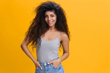 Sarı arka planda izole edilmiş, kameraya bakan yakışıklı Latin kadının portresi. Elleri ceplerinde ve üstünkörü giyinmiş, gülen beyaz kadın. Mutlu kadın model gülümsüyor