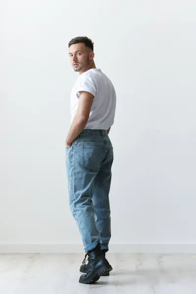 Full body view from the back shot of handsome serious tanned man guy in basic t-shirt looks at camera posing on white background. Fashion Style New Collection Offer. Copy space for ad. Model snap
