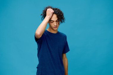 Basit tişörtlü yakışıklı, bronz tenli beyaz adam mavi arka planda izole edilmiş kafaya dokunuyor. Yaşam tarzı ve Duygular konsepti. Reklam için fotokopi alanı için iyi teklif.