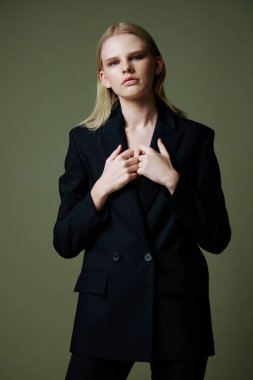 Model, stüdyoda yeşil bir arka planda poz verirken ceketi yakasından tutuyor. Kıyafet markaları için konsept fotoğraf. Şık takımlar için harika bir teklif. Yüksek kalite fotoğraf