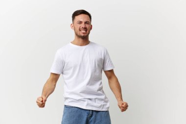 Çığlık atan, kızgın, bronzlaşmış, basit tişörtlü yakışıklı adam beyaz stüdyo arka planında izole edilmiş yumruklarını sıkıyor. Uzayın afiş modelini kopyala. İnsanların duyguları Yaşam tarzı konsepti