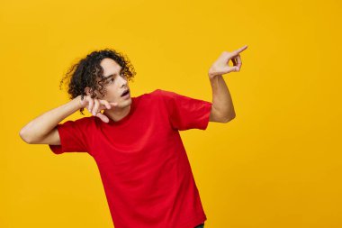 Kırmızı tişörtlü komik beyaz adam sarı stüdyo arka planında yalnız poz veriyor. Reklamcılık için bedava olan en iyi teklif. Günlük kavramlar için duygular