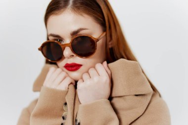 Palto mağazası için afiş. Gözlüklü genç kızıl saçlı bir kız stüdyoda beyaz bir arka planda ceket tasması tutuyor. Katalog fotoğrafçılığı. Yüksek kalite fotoğraf