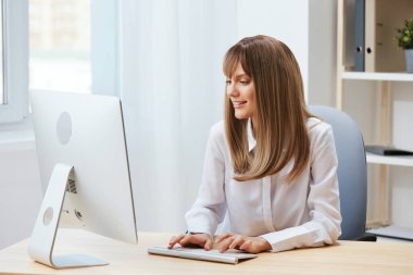 Neşeli, mutlu, tapılası sarışın iş kadını serbest çalışan biri açık modern ofisteki masaüstü bilgisayarında ekran çalışmalarına bakıyor. Üç aylık rapor yazan mutlu bir çalışan. Boşluğu kopyala, uzak görev