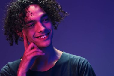 Siyah tişörtlü neşeli kıvırcık adam pembe mavi stüdyo arka planında yalnız poz veriyor. Güzel moda teklifi. Sanal Gerçeklik Yeni Koleksiyon konsepti. İlan için alanı kopyala