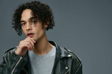 Seksi, şık, bronzlaşmış, kıvırcık deri ceketli adam gri stüdyo arka planında izole edilmiş kameraya bakıyor. Güzel moda teklifi. Büyük Mevsimlik Satış Yeni Koleksiyon konsepti. İlan için alanı kopyala