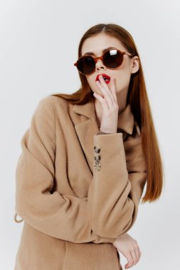 Kendine güveni tam kızıl saçlı, ceketli ve gözlüklü bir kız stüdyoda beyaz arka planda poz veriyor. Dergi için reklam katalogu çekimi. Yüksek kalite fotoğraf