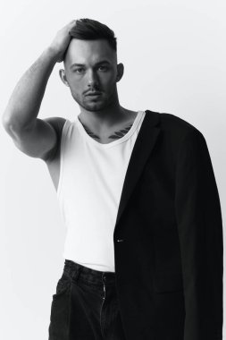 Fotoğrafları modelliyorum. Kendine güveni olan, ceketli, tek omuzlu, yakışıklı bir adam beyaz stüdyo arka planında yalnız poz veriyor. Siyah ve Beyaz konsepti. Moda teklifi. Boşluğu kopyala