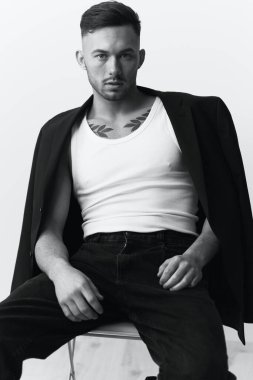 Fotoğrafları modelliyorum. Kendine güveni olan, siyah ceketli, beyaz stüdyo arka planında oturan yakışıklı bir adam. Siyah ve Beyaz konsepti. Boşluğu kopyala