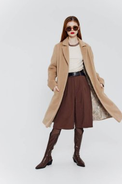 Stüdyoda beyaz bir arkaplanda poz veren bej gözlüklü kızıl saçlı şık bir bayan. Yüksek kalite fotoğraf