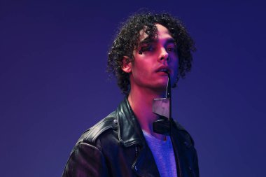 Cilveli kıvırcık deri ceketli şık bir erkek gözlüklü pembe mavi stüdyo arka planında izole bir şekilde poz vermene bakıyor. Güzel moda teklifi. Büyük Mevsimlik Satış Yeni Koleksiyon konsepti. İlan için alanı kopyala