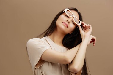 Gözlüklü, bej tişörtlü, giyinik, izole bir arka planı olan genç bir kadın. Yüksek kalite fotoğraf