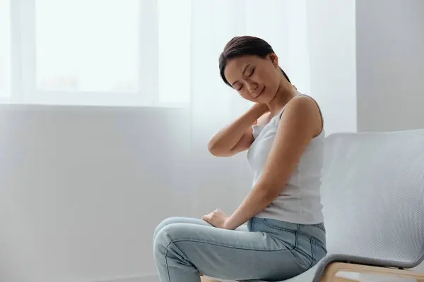 Neck pain. Suffering from fibromyalgia tanned beautiful young Asian woman rubbing massaging tensed muscles at home interior living room. Injuries Poor health Illness concept. Cool offer Banner