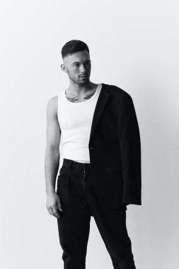 Fotoğrafları modelliyorum. Kendine güveni tam, ceketli yakışıklı bir adam beyaz stüdyo arka planında yalnız poz veriyor. Siyah ve Beyaz konsepti. Moda teklifi. Boşluğu kopyala