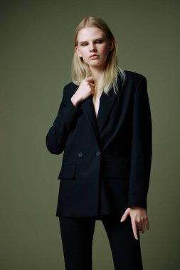 Sarışın bir kadın, stüdyoda yeşil bir arka planda poz veren bir ceketi yakasından tutuyor. Giysi markaları için bir konsept. Şık takımlar için harika bir teklif. Yüksek kalite fotoğraf