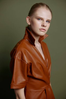 Mevsimlik indirim teklifi. Kendine güveni tam, deri ceketli genç bir bayan zeytin yeşili stüdyo arka planında izole edilmiş akşam makyajını gösteren mavi gözlü bir kadın.